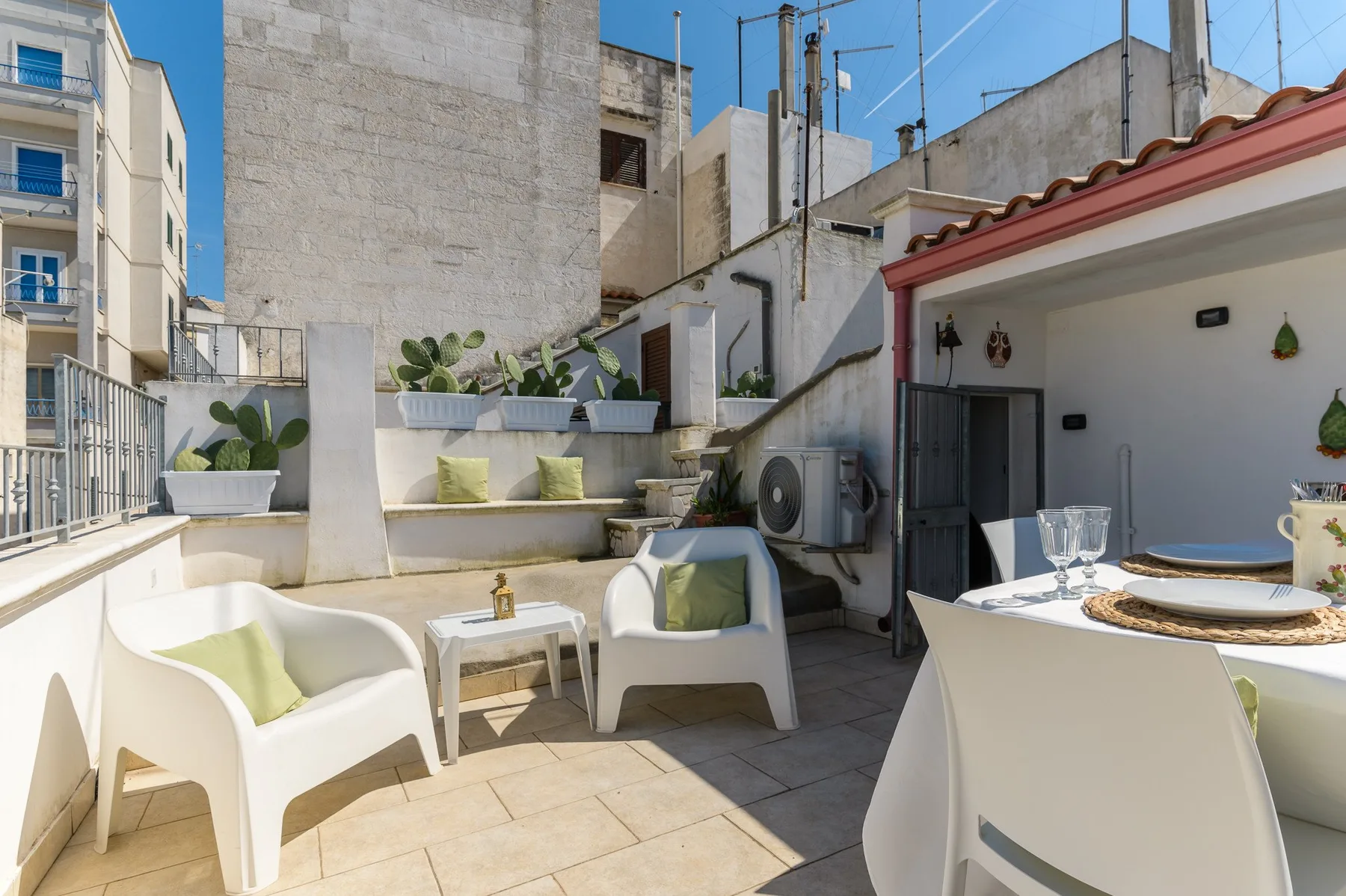 A rooftop terrace with white seating, potted plants, and an outdoor dining table.
