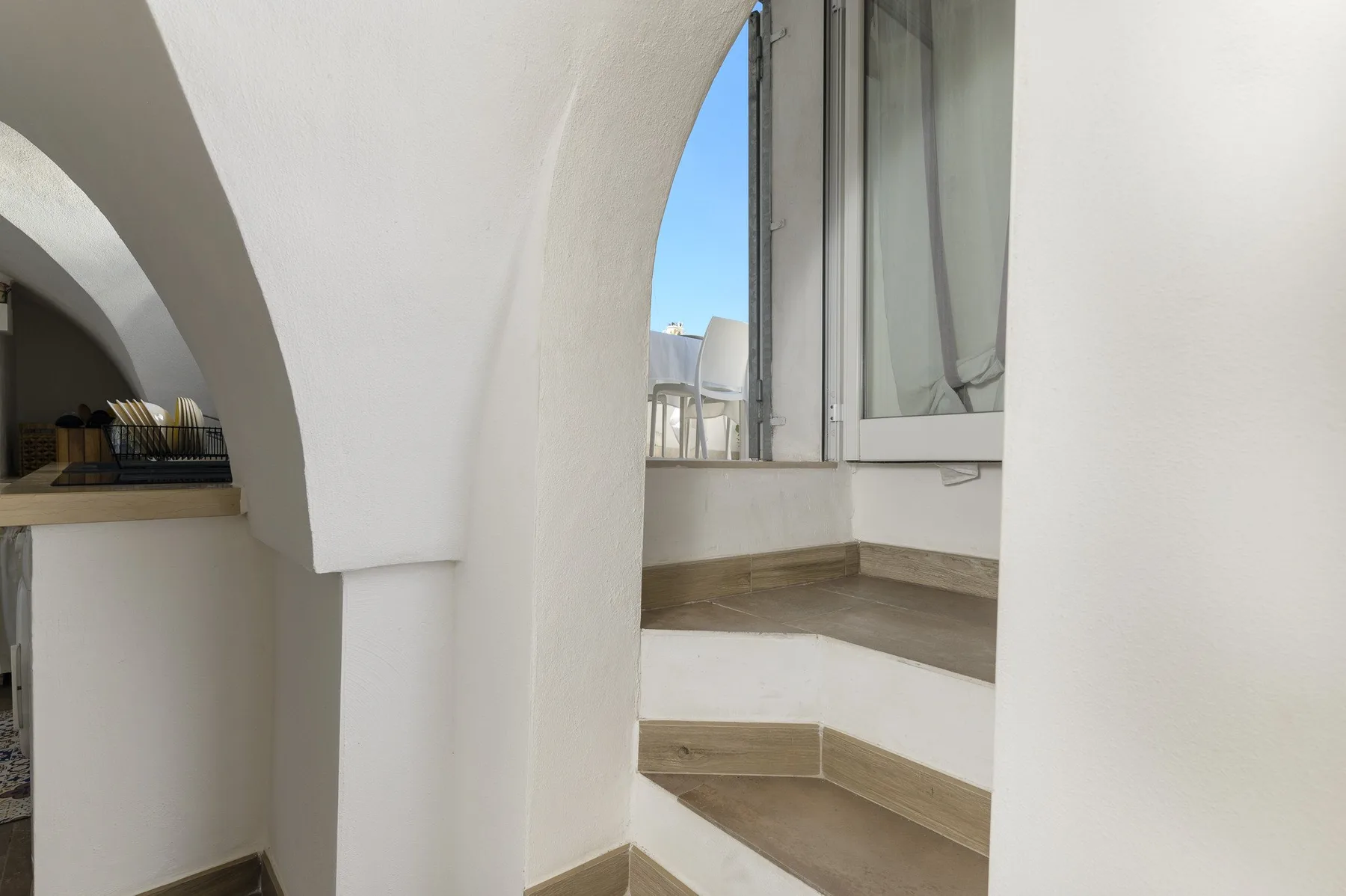 A bright interior stairway curves beside an arched opening and a window.