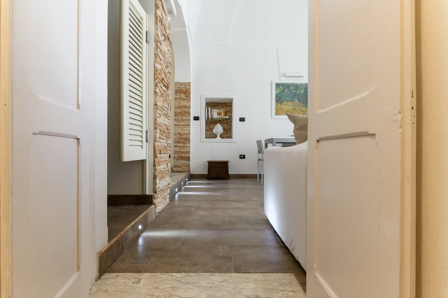 A bright living room is visible through an open doorway, with seating and a stone wall.