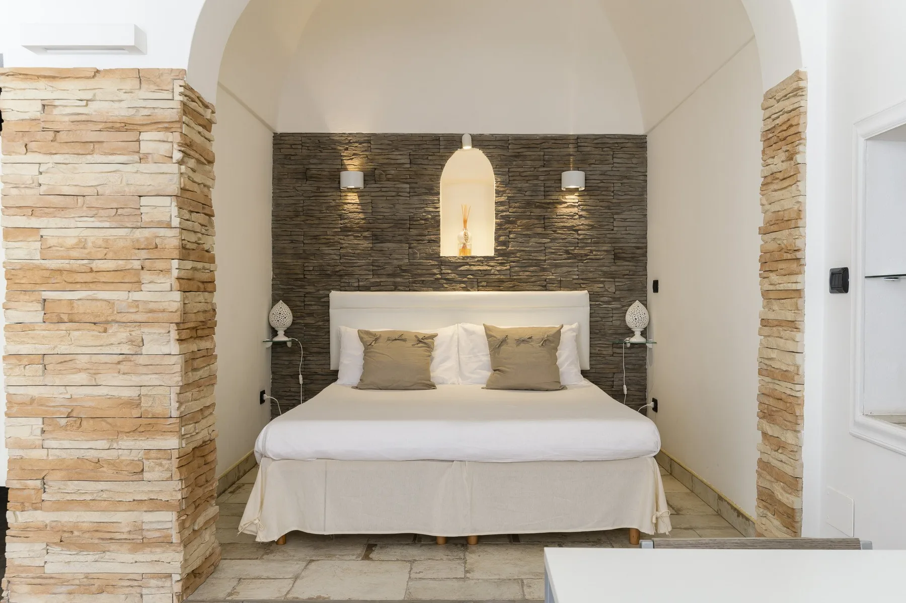 A bedroom with a neatly made bed beneath a recessed wall niche.