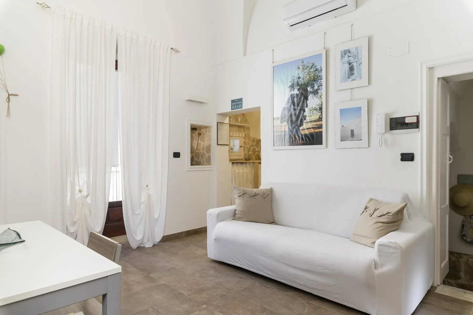 A bright sitting room with a white sofa and framed artwork on the wall.