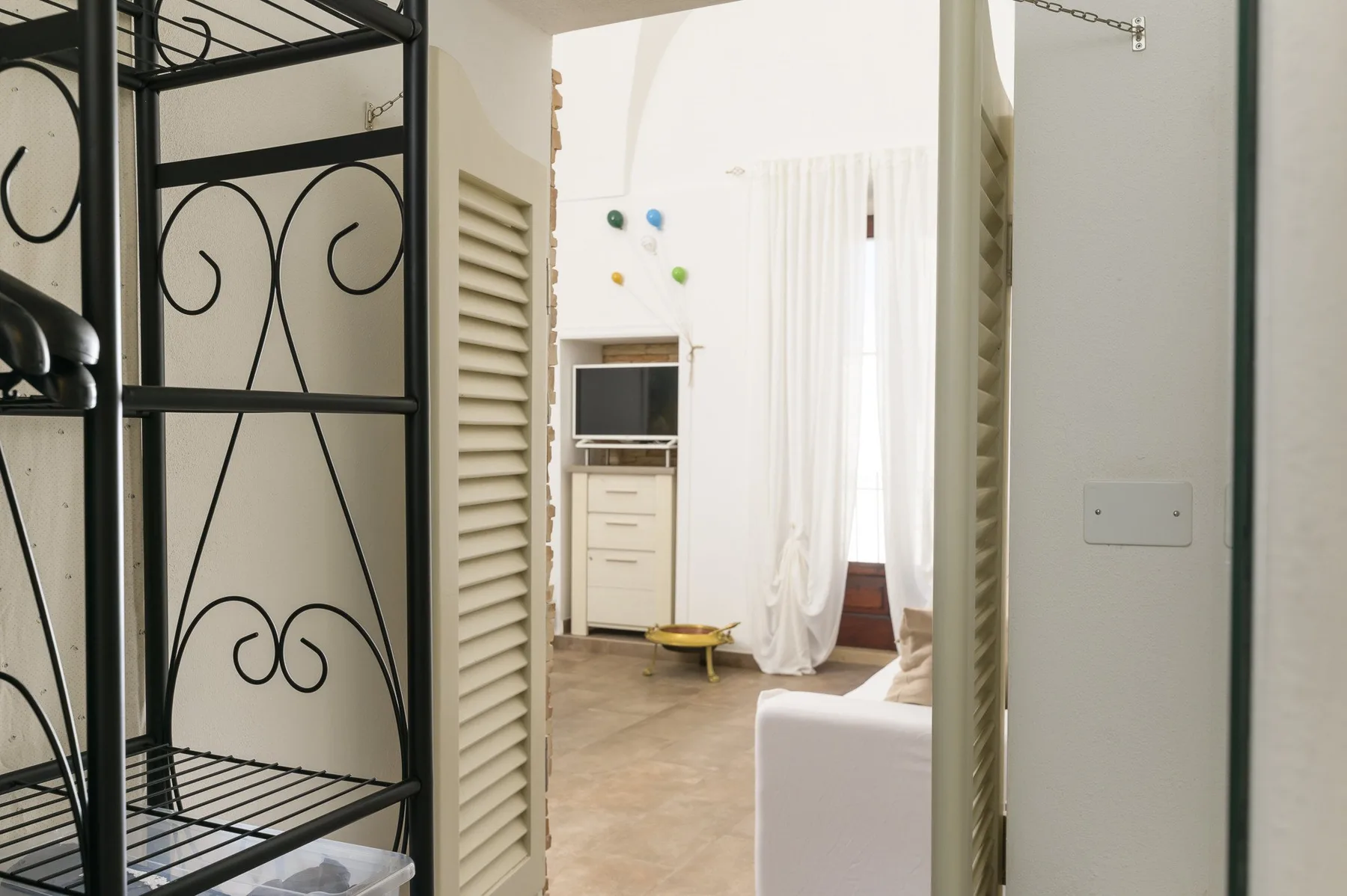 A bright room with a television cabinet and white curtains beside an open doorway.