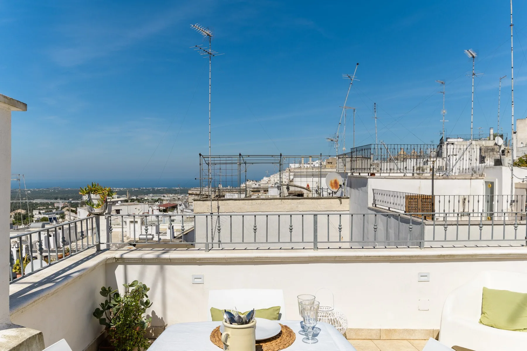 A rooftop terrace with a table and chairs overlooks nearby buildings and the distant coastline.