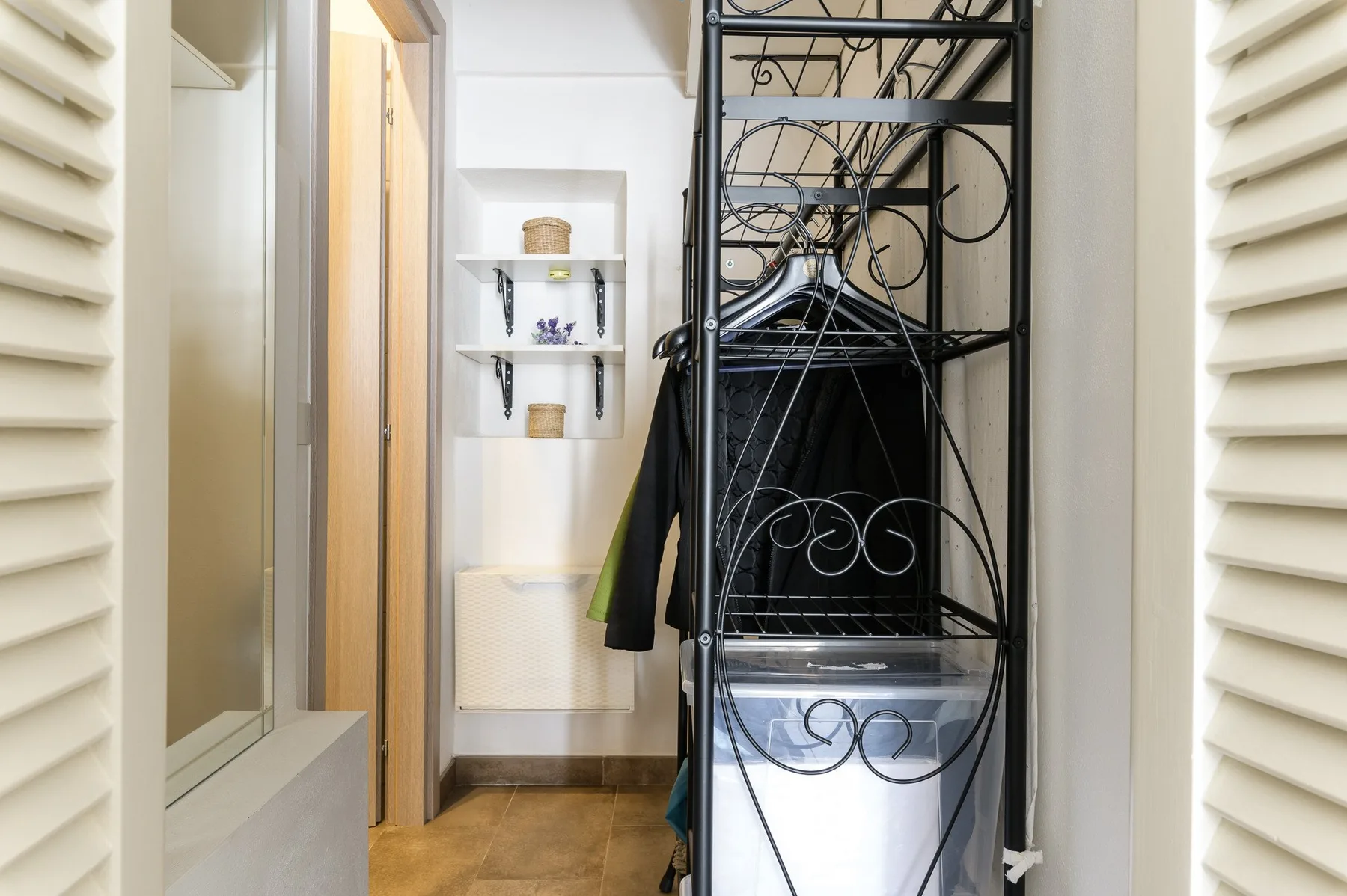 A narrow interior passage with a black metal clothing rack and a recessed shelf.