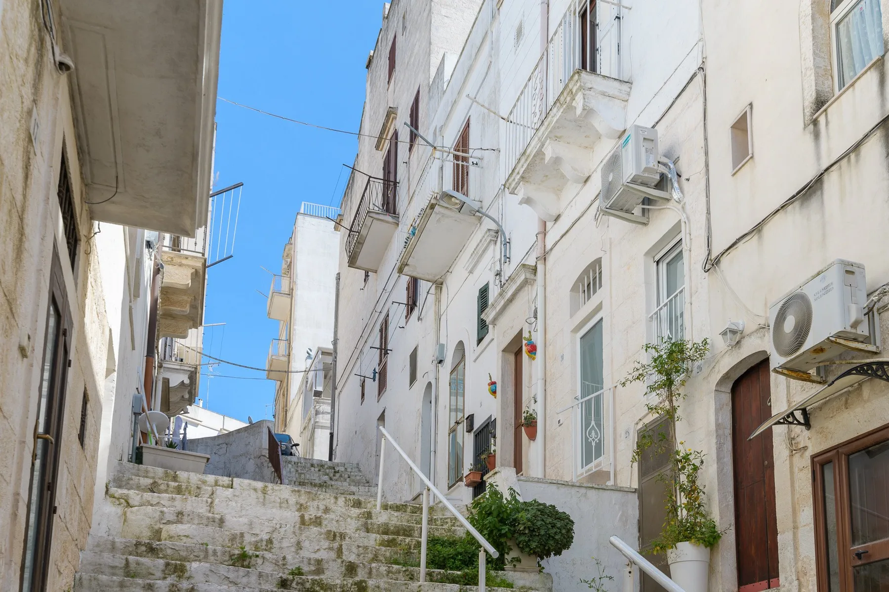 A narrow outdoor stairway runs between white buildings beneath a clear blue sky.
