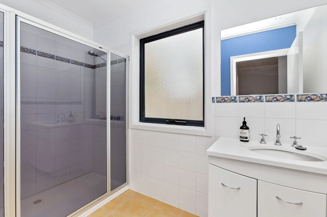 Un baño con una ducha alicatada y un lavabo bajo una ventana.