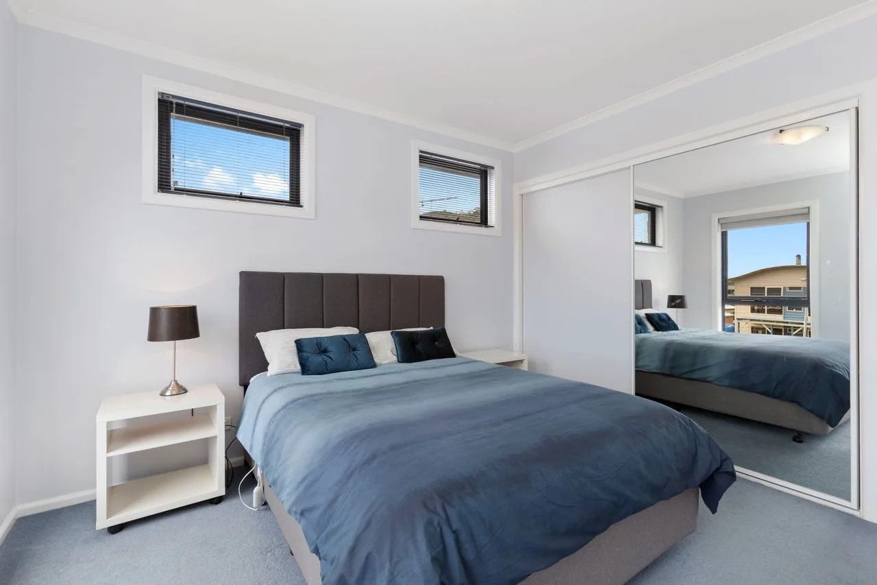A bedroom with a bed and mirrored wardrobe doors.