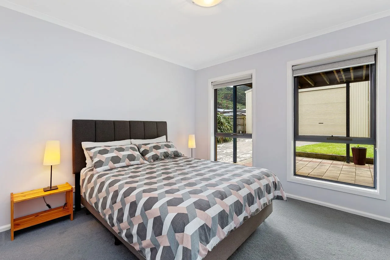 A bedroom with a made bed beside two windows.