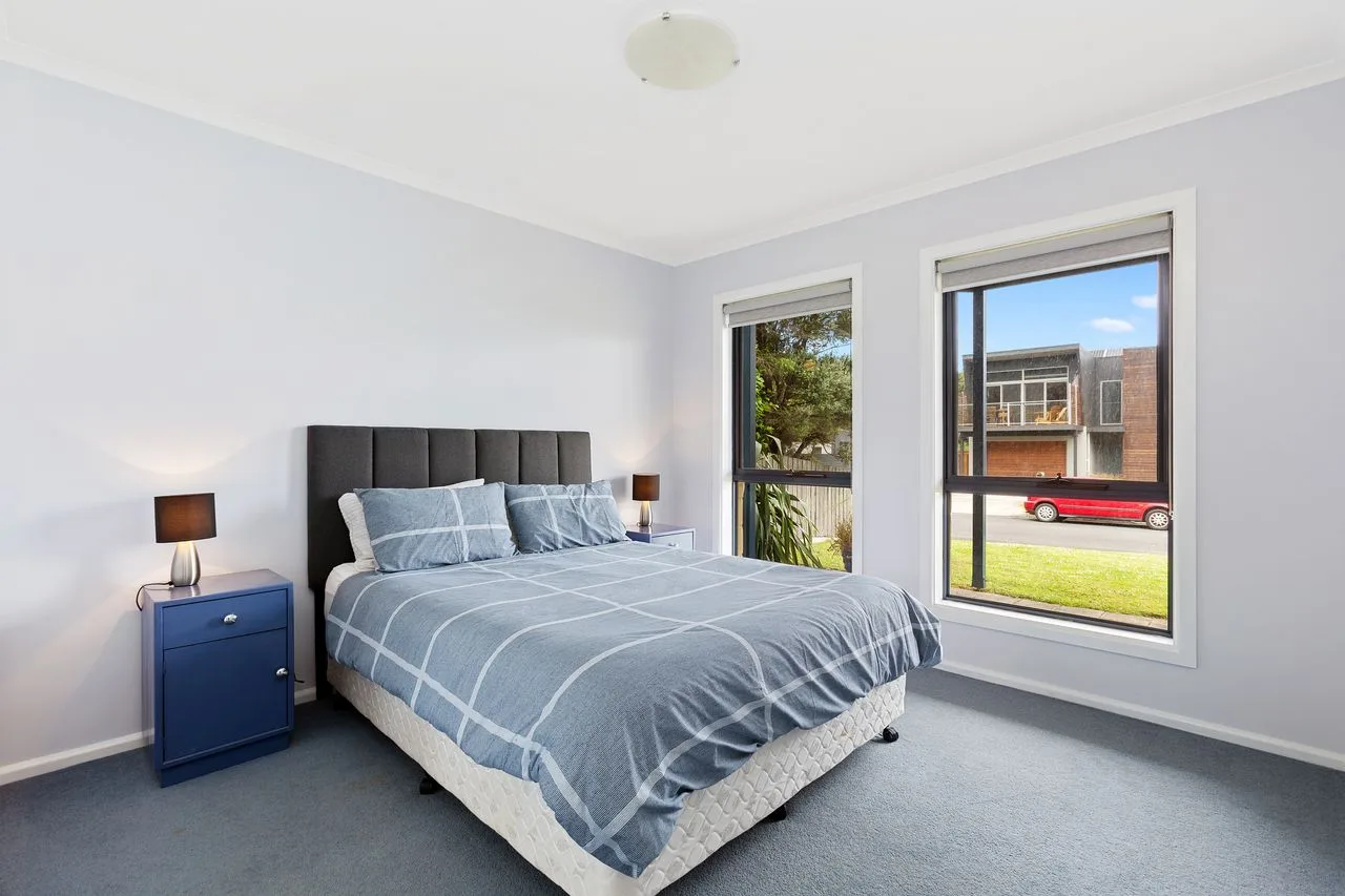 Un dormitorio con una cama, ropa de cama azul y dos ventanas grandes.