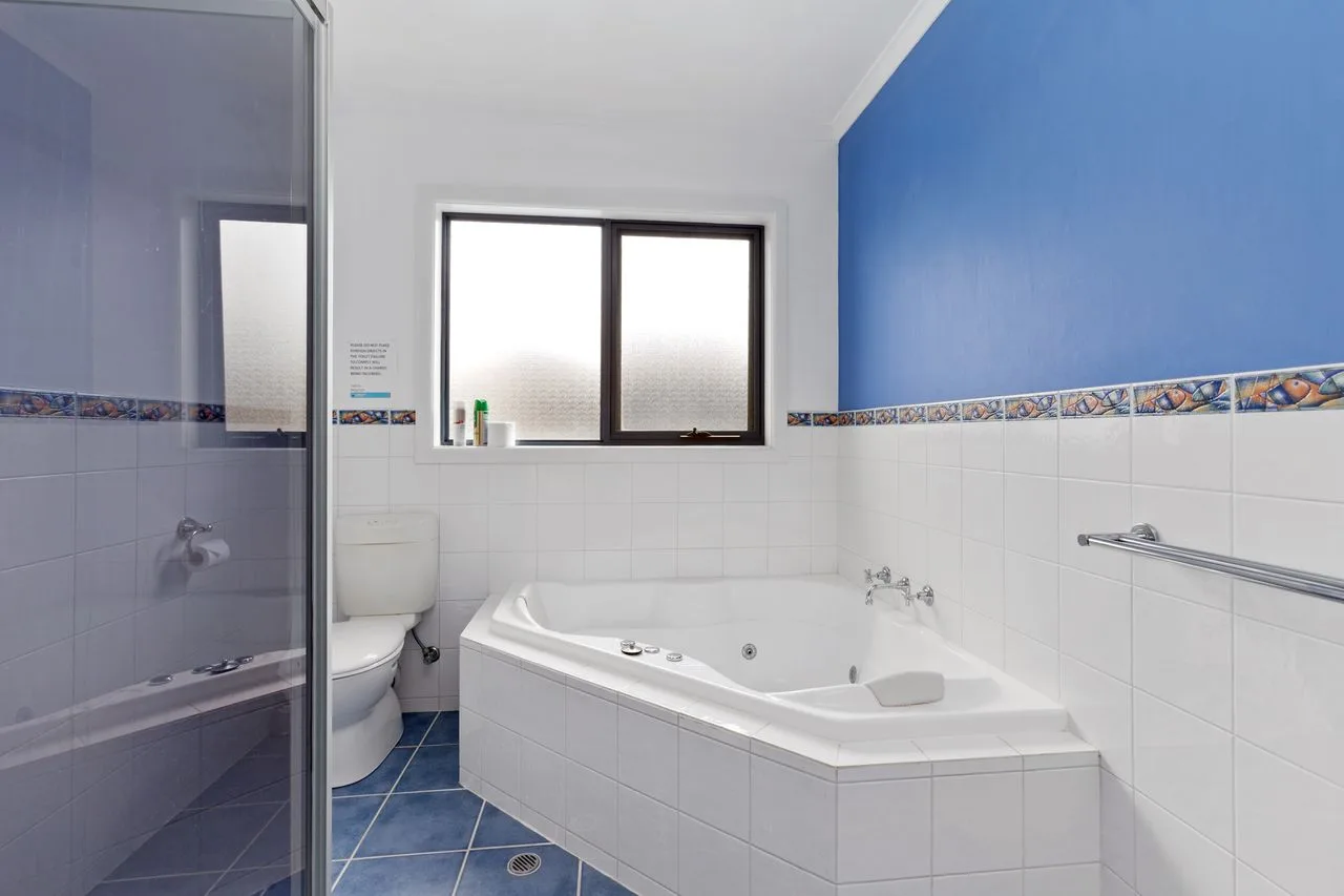 Un baño alicatado con una bañera de esquina y una ventana esmerilada.