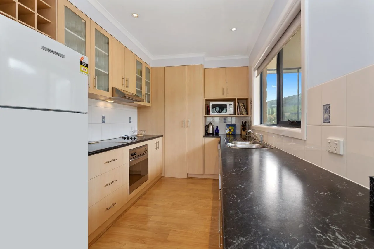 Una cocina luminosa con gabinetes de madera clara y una larga encimera oscura.