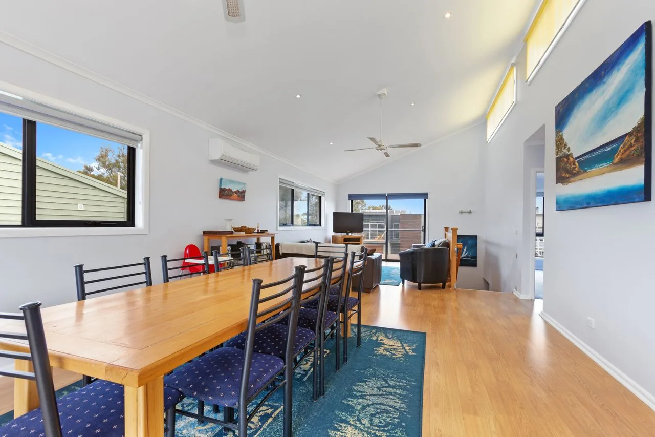 Una luminosa zona de comedor y estar con una larga mesa de madera y asientos.