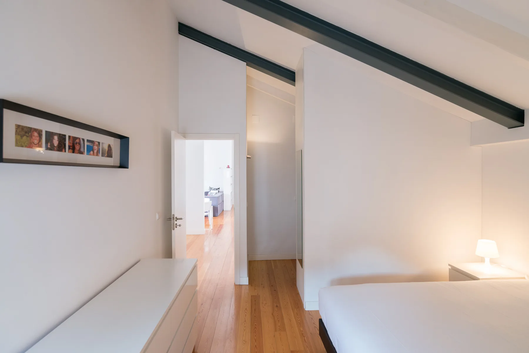 Dormitorio luminoso con una cama, una cómoda baja y una puerta al pasillo.