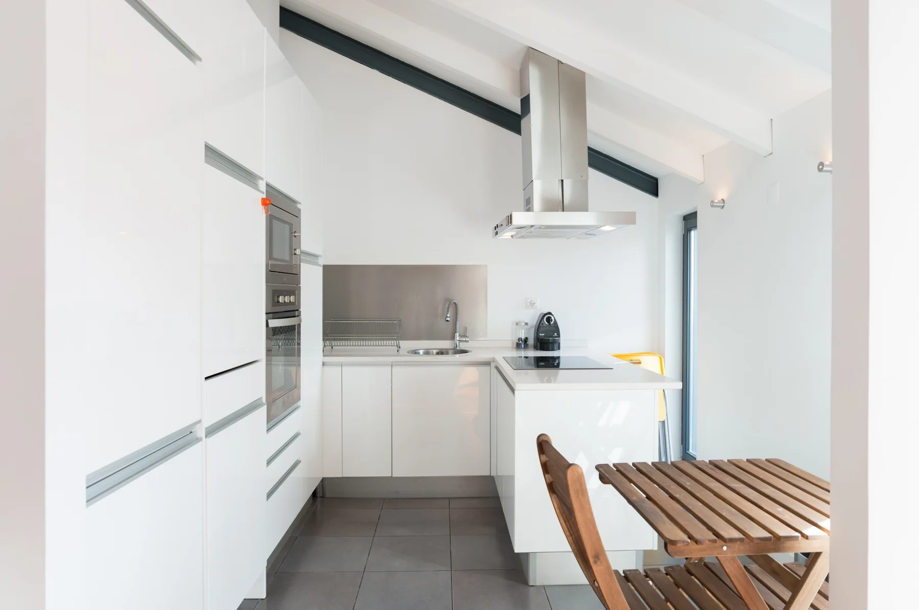 Una cocina luminosa y moderna con armarios blancos y una mesa de comedor de madera.