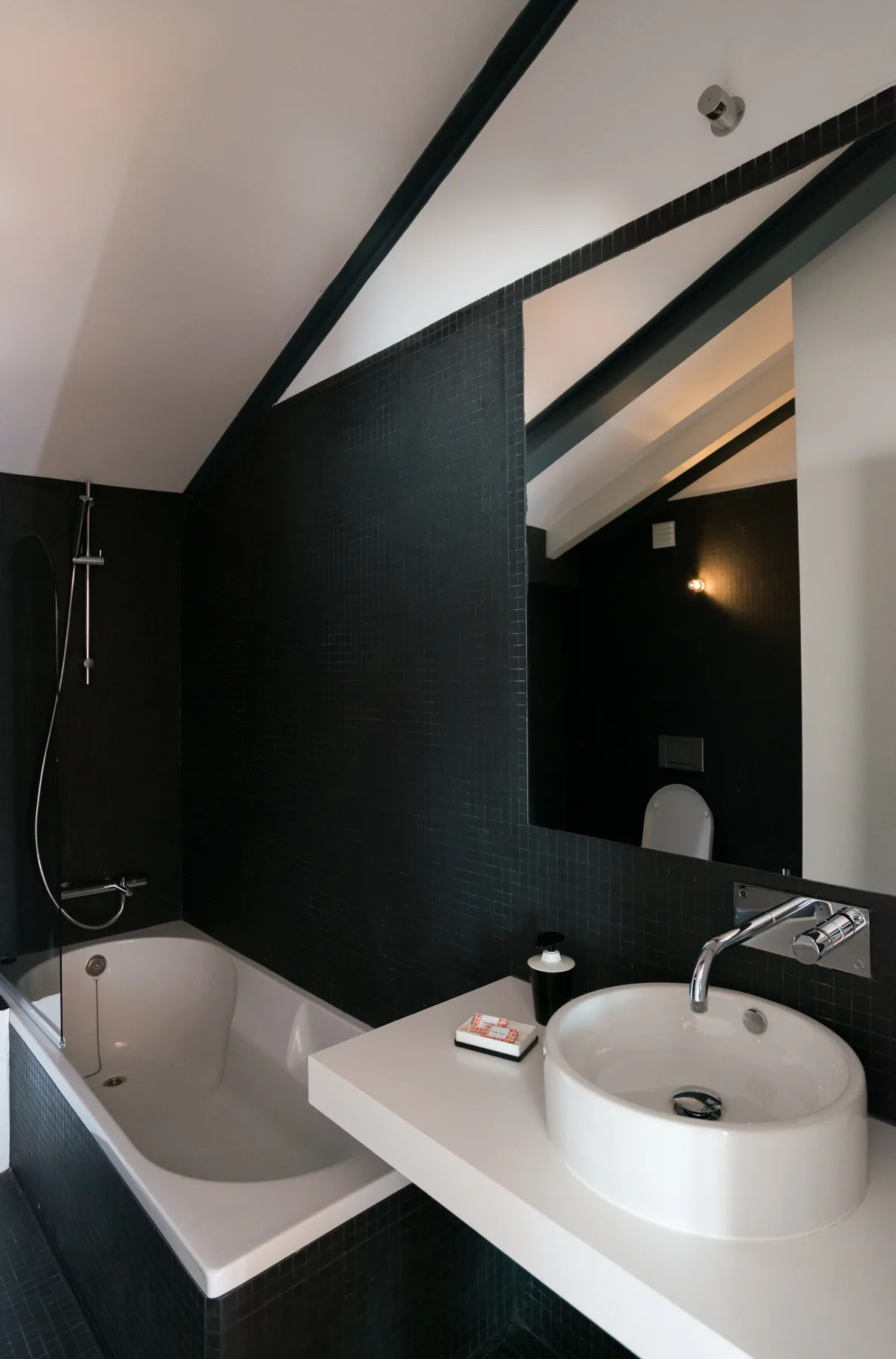 Un baño con azulejos oscuros, bañera, lavabo y un espejo grande.