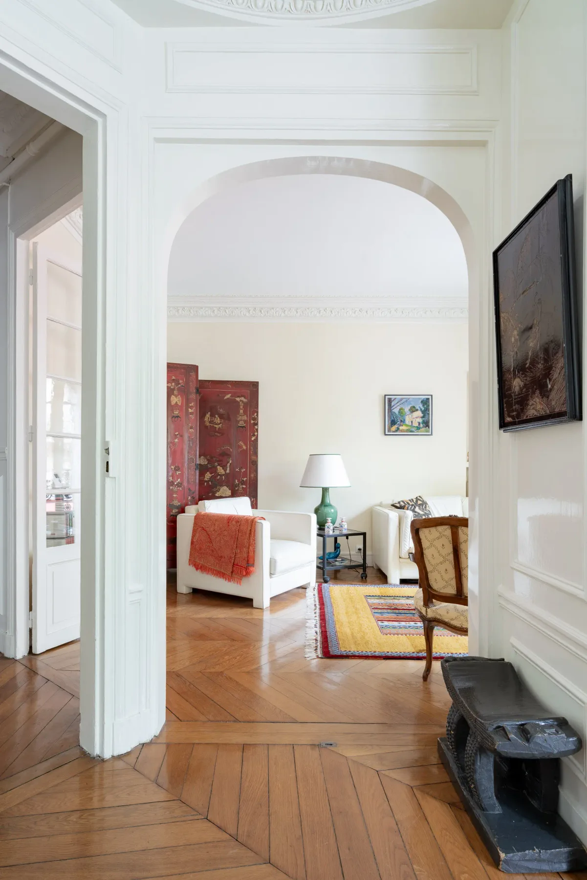 Una sala de estar luminosa con asientos blancos y una alfombra colorida bajo un arco.