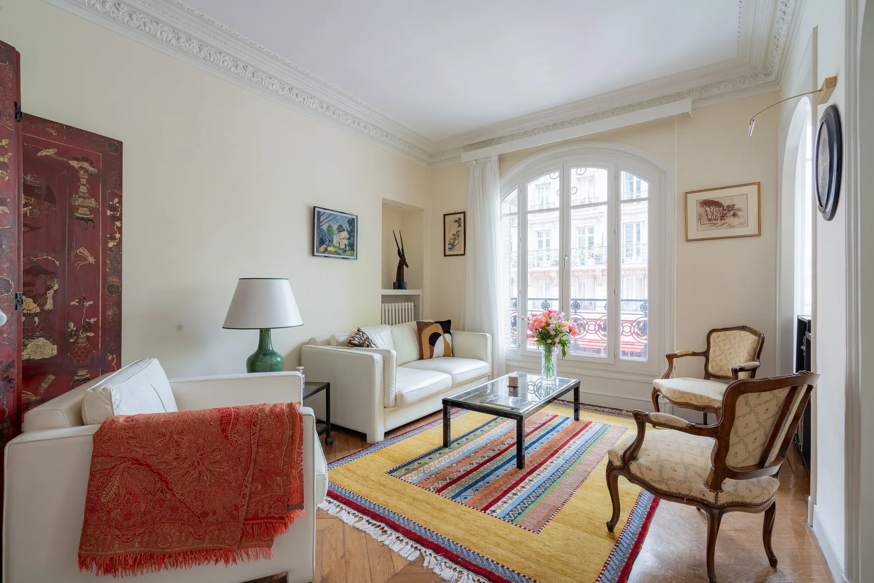Una sala luminosa con asientos alrededor de una alfombra colorida y una gran ventana arqueada.