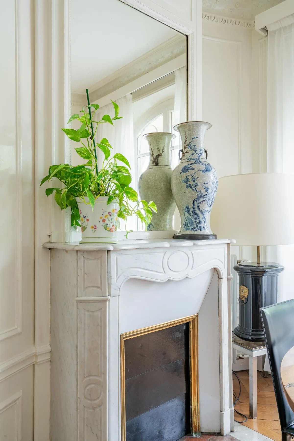 Una sala luminosa presenta una chimenea blanca, un espejo y una planta frondosa.