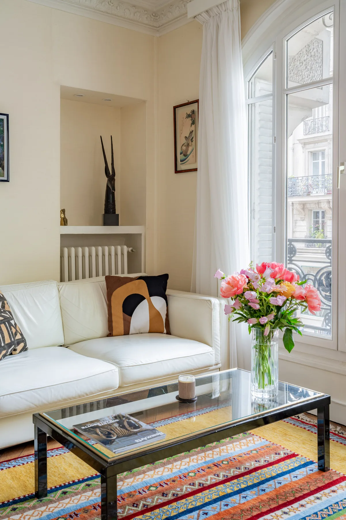 Una sala luminosa con asientos blancos, una mesa de centro de vidrio y flores junto a la ventana.