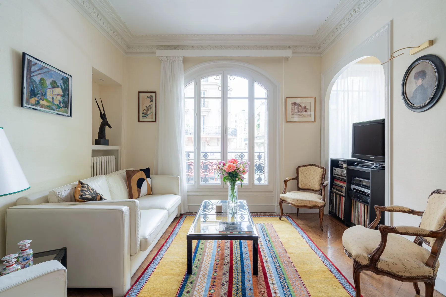 Una sala luminosa con un sofá, una mesa de centro de vidrio y una gran ventana arqueada.