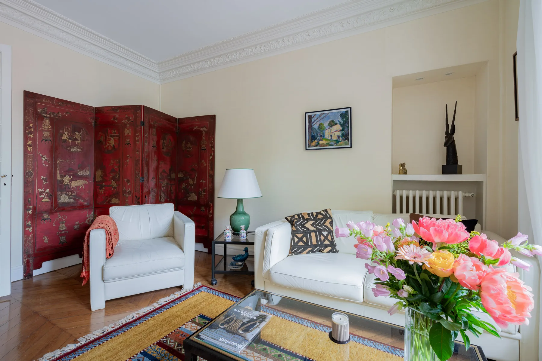 Una sala luminosa tiene asientos blancos, un biombo rojo y un arreglo floral.