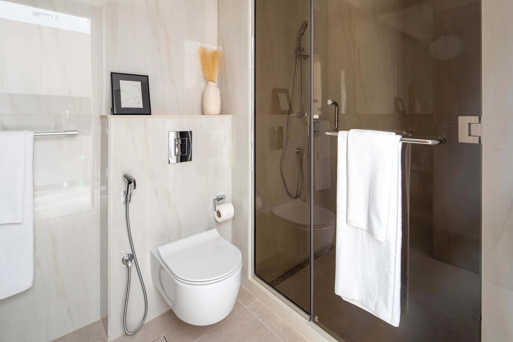 Un baño luminoso con azulejos, un inodoro suspendido y una ducha de vidrio.