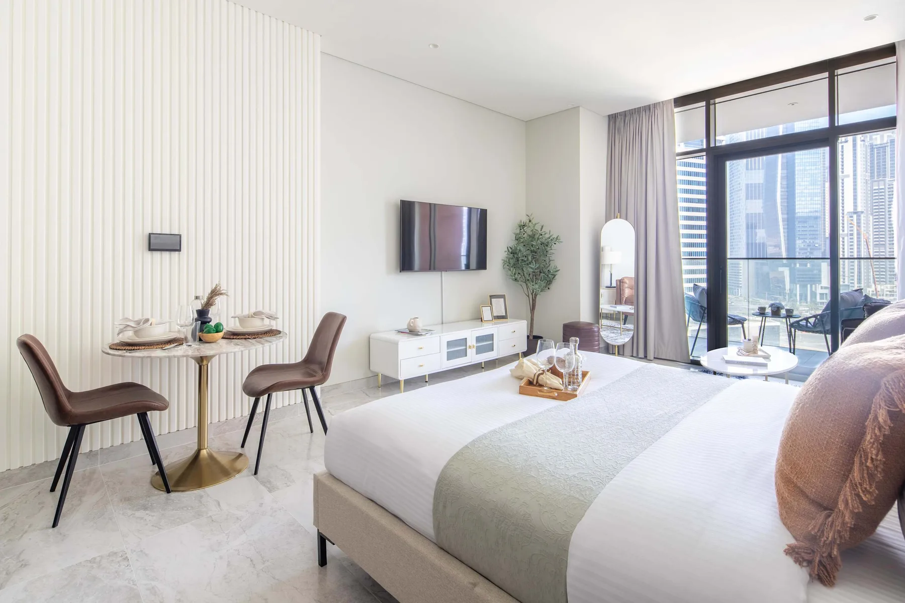 Un dormitorio luminoso con una cama grande, una mesa y ventanas de piso a techo.