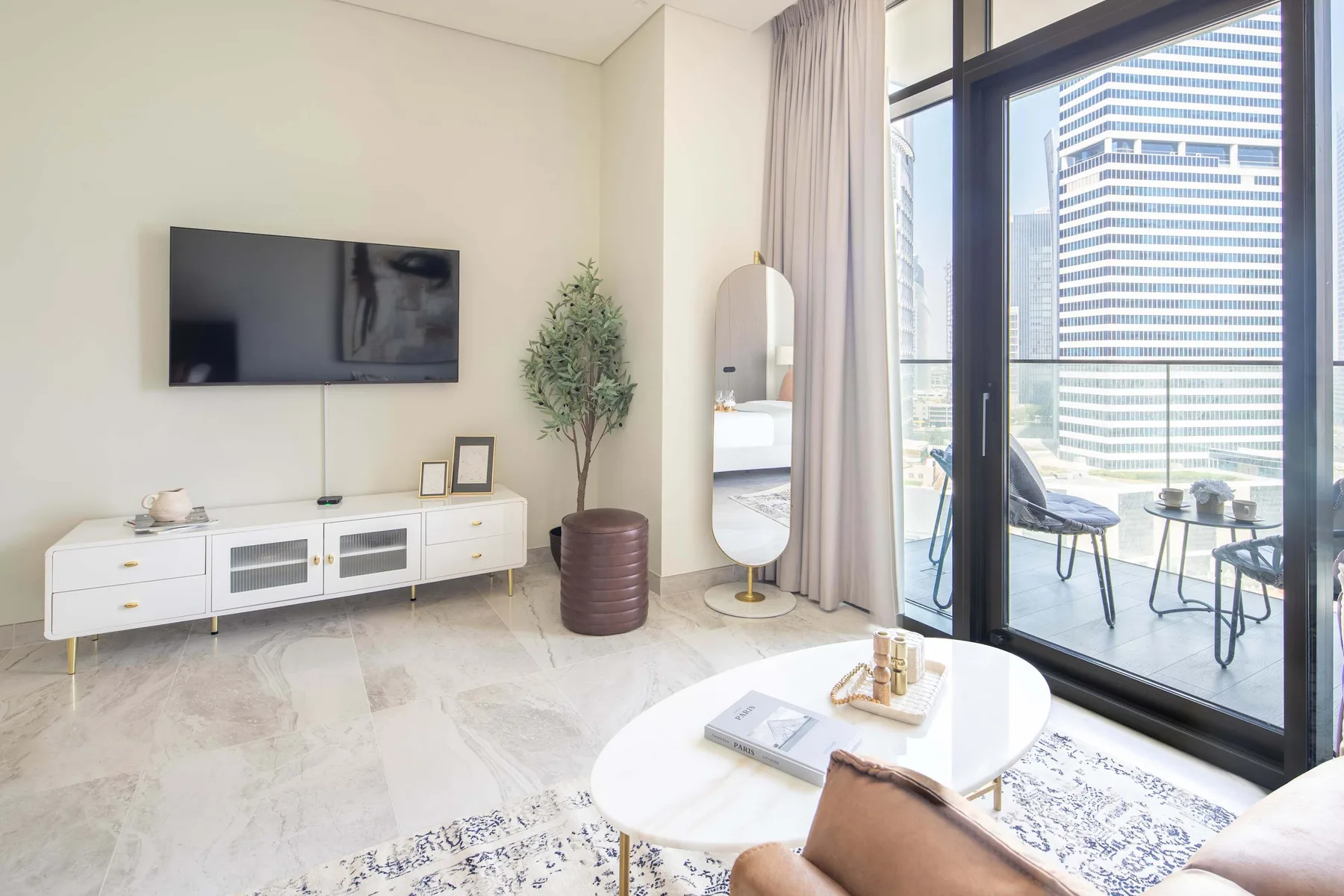 Una sala luminosa con televisor, mueble bajo y ventanales de piso a techo.