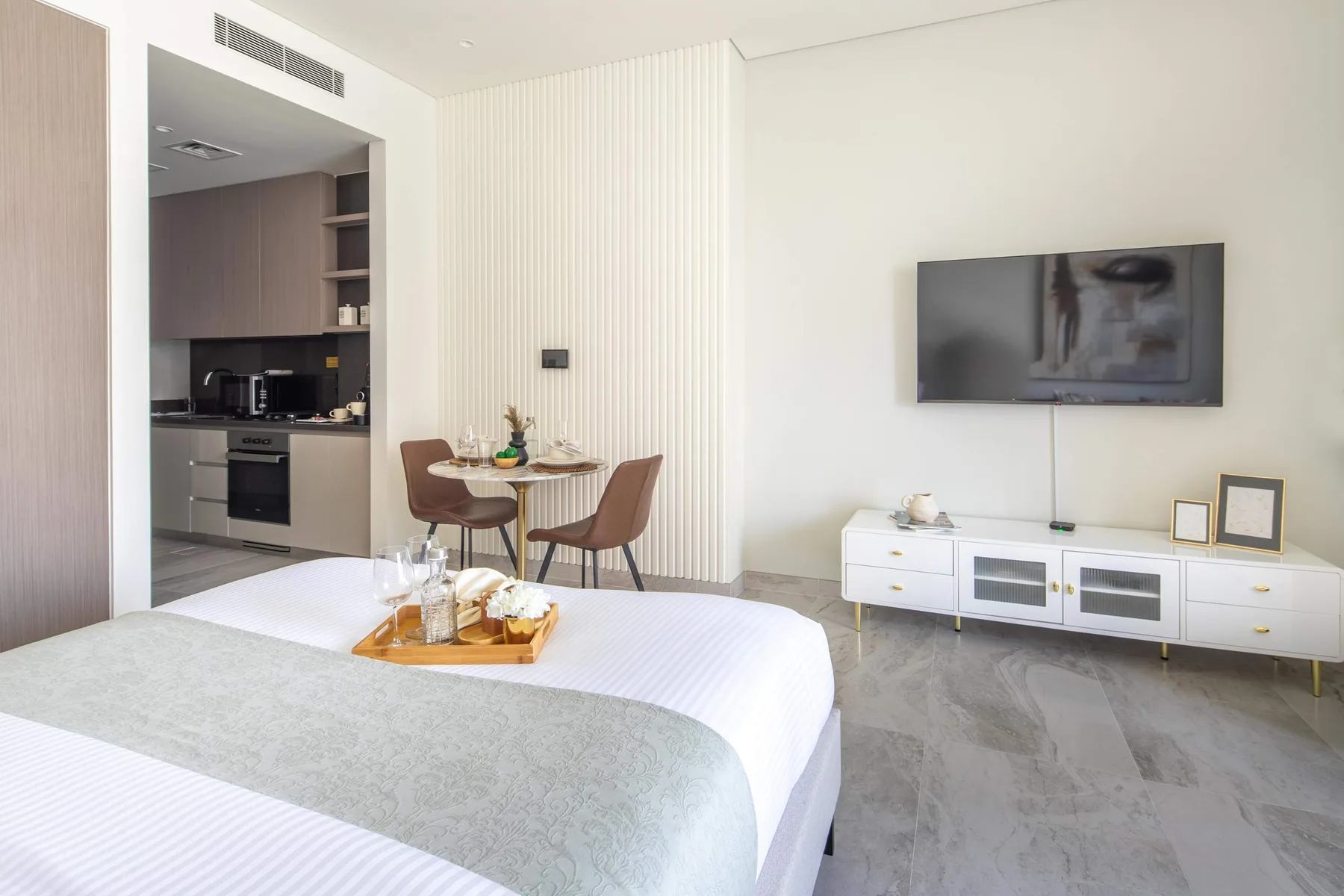 Un dormitorio luminoso con una cama bien hecha, un televisor en la pared y un rincón de comedor.