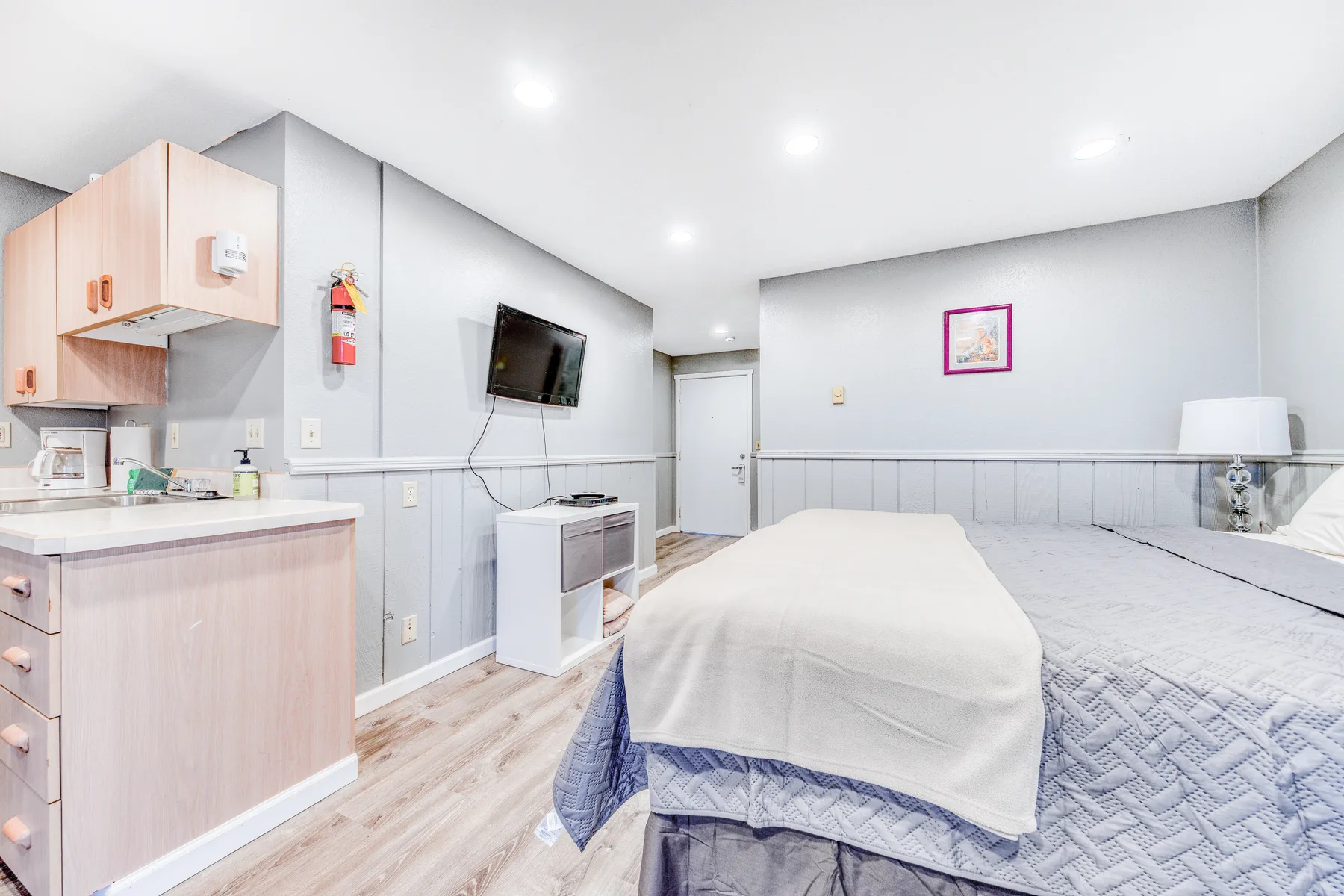 Un dormitorio con una cama grande, una pequeña cocina y un televisor montado en la pared.