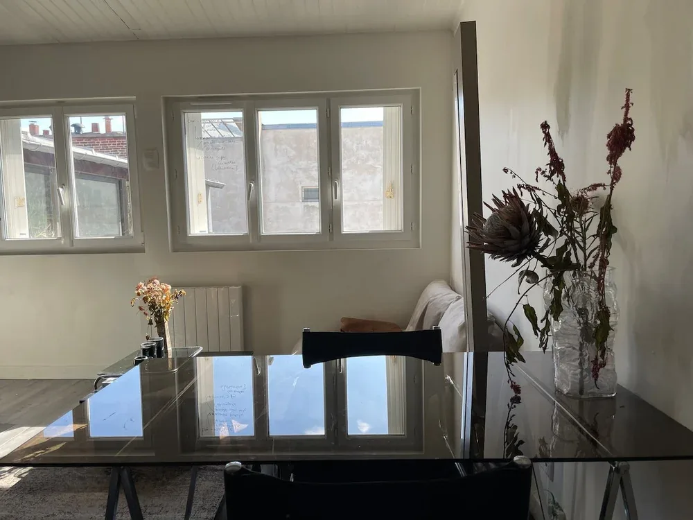 A dining area with a glass table and windows along the wall.