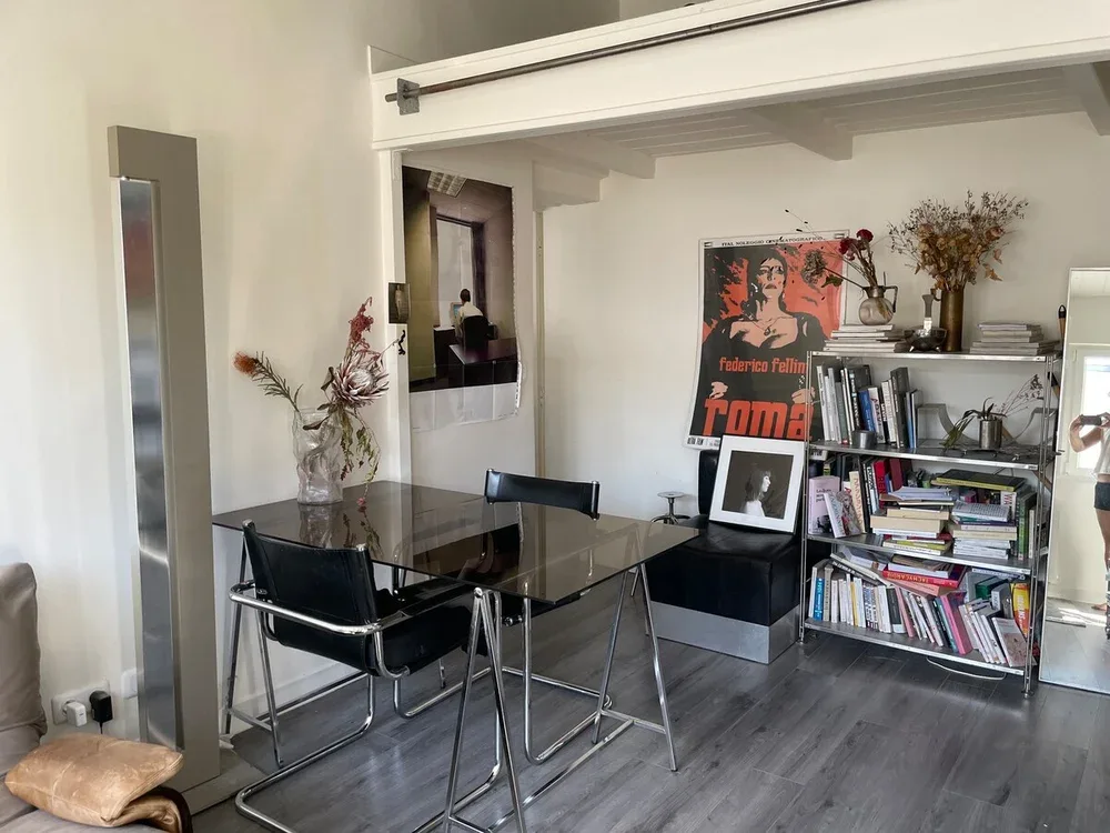 A dining and living area with a glass table, seating, and bookshelves.