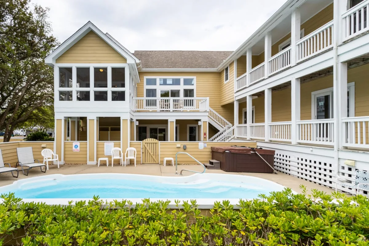 Una piscina está junto a una casa grande amarilla con balcones blancos.