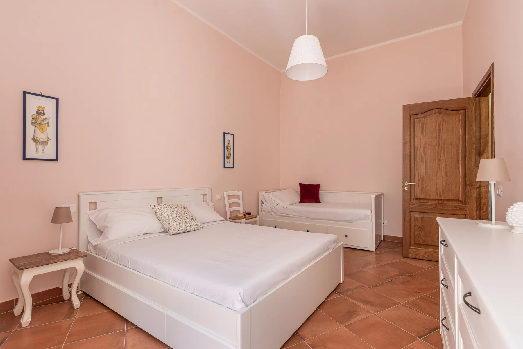 A pink bedroom with a large bed, a small sofa, and a wooden door.