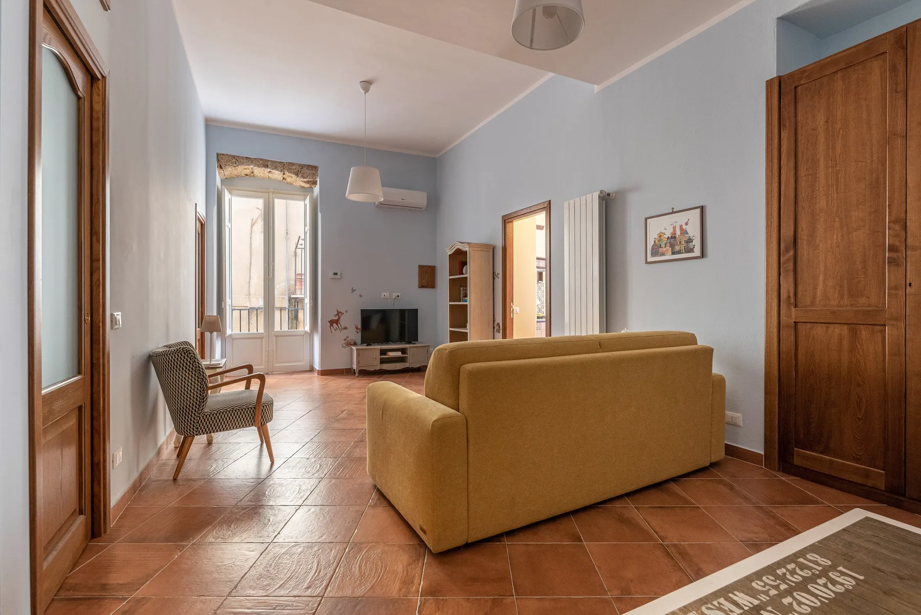 A living room with seating, a television, and a glass door opening to a balcony.
