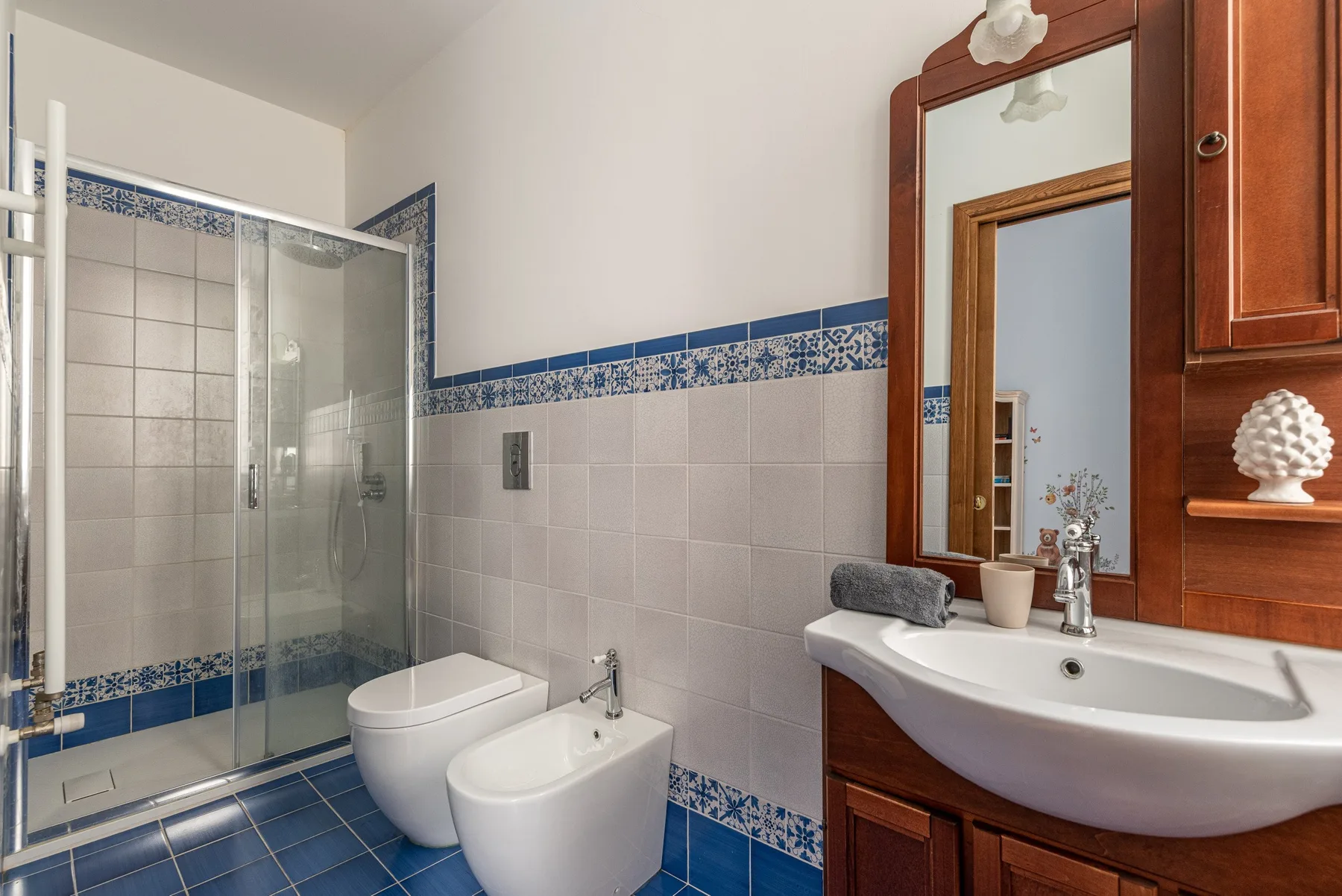 A tiled bathroom with a glass shower, toilet, and sink beneath a mirror.