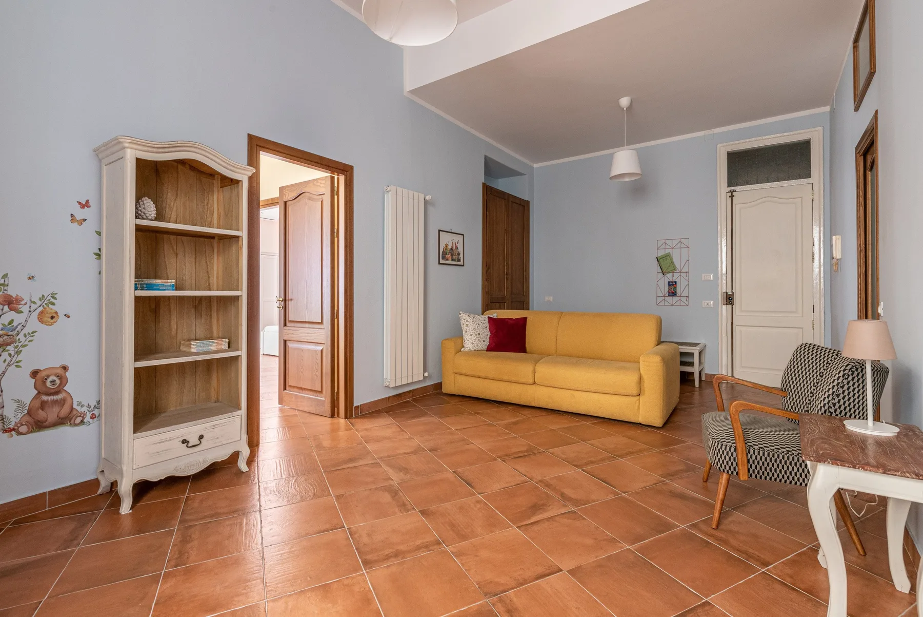 A living room with a yellow sofa and tiled floor.