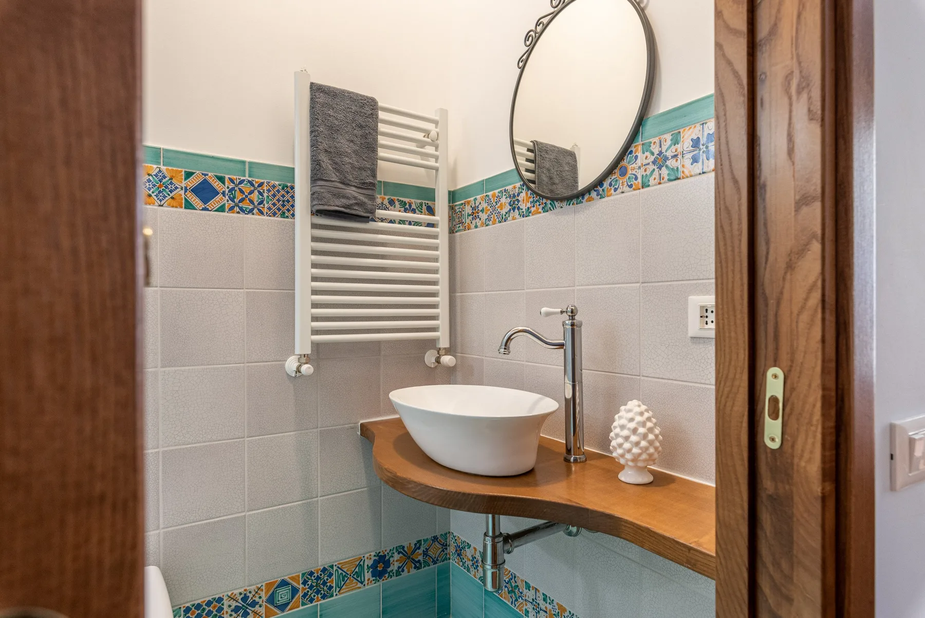 A bathroom vanity with a white vessel sink, wall mirror, and tiled walls.