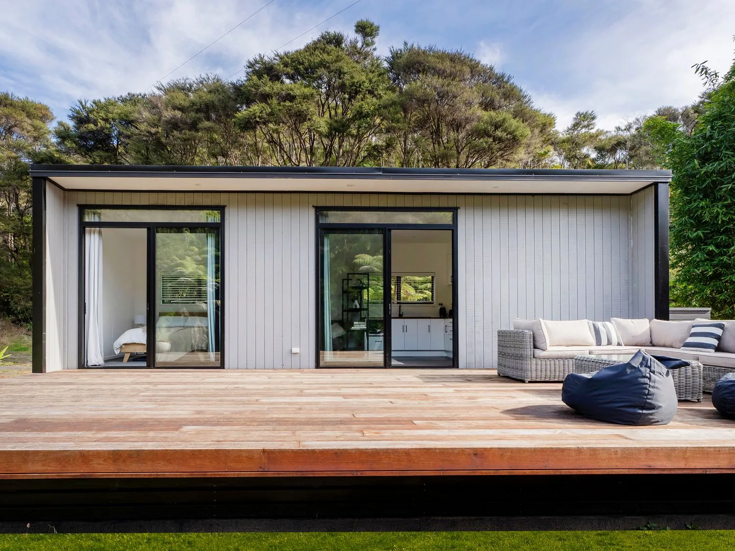 A wooden deck with outdoor seating and bean bags sits in front of a cabin with large glass doors.