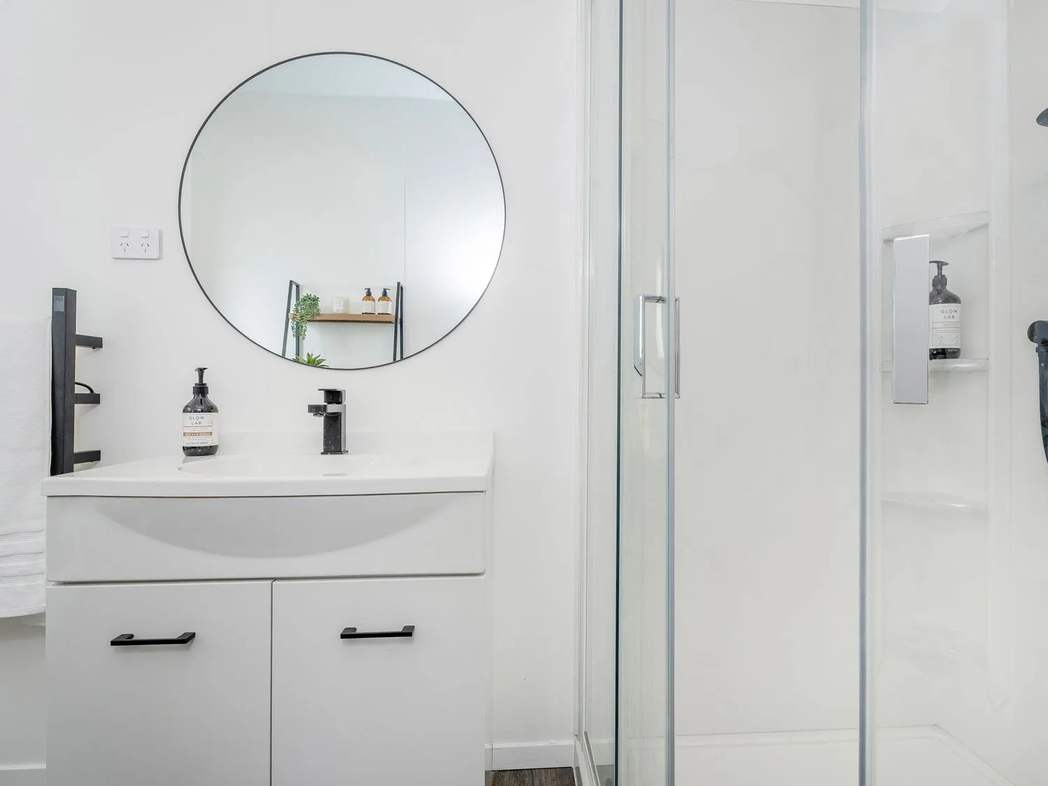 A bathroom with a white vanity, round mirror, and glass shower.