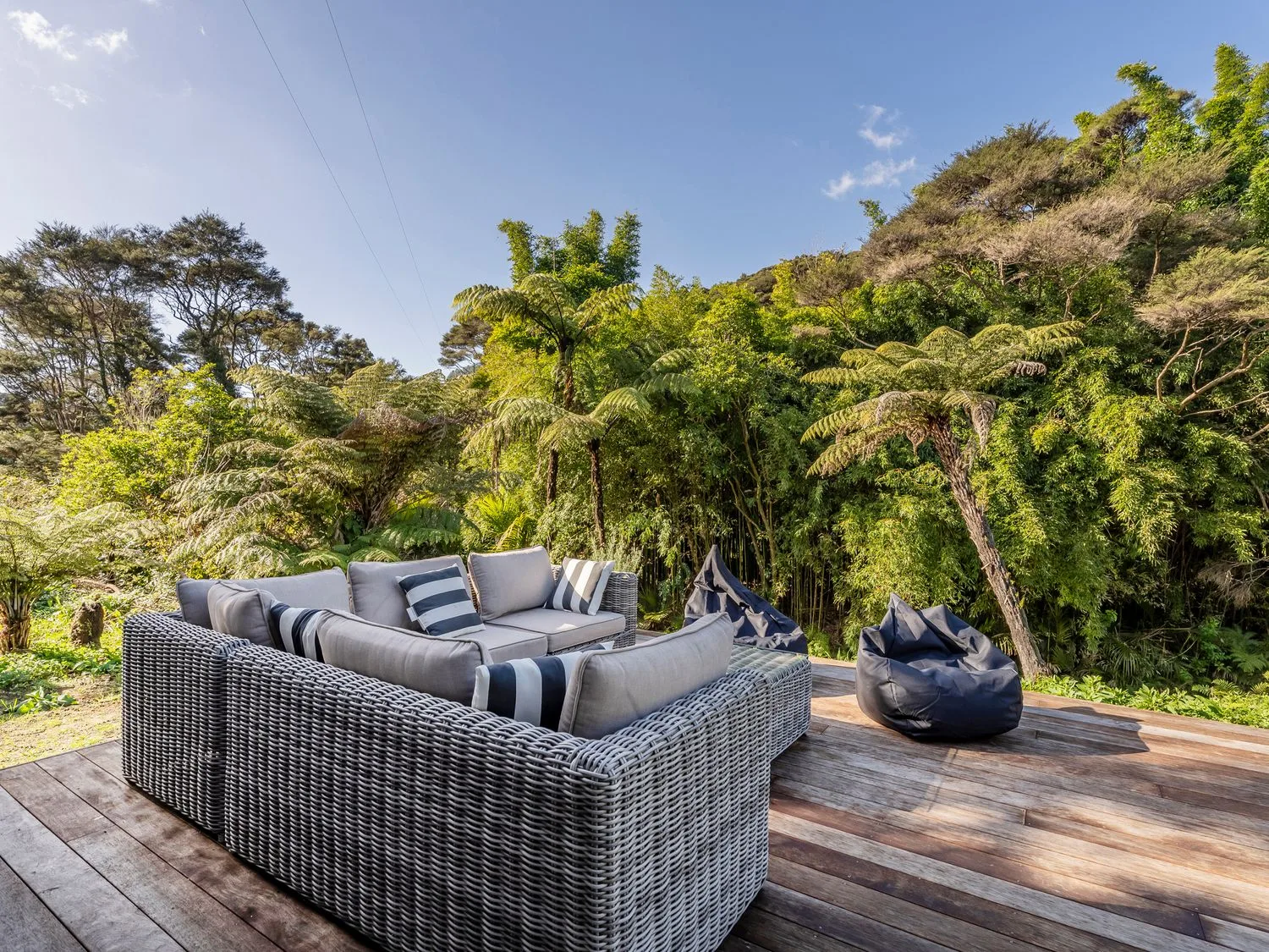 Zona de estar al aire libre en una terraza de madera, rodeada de vegetación.