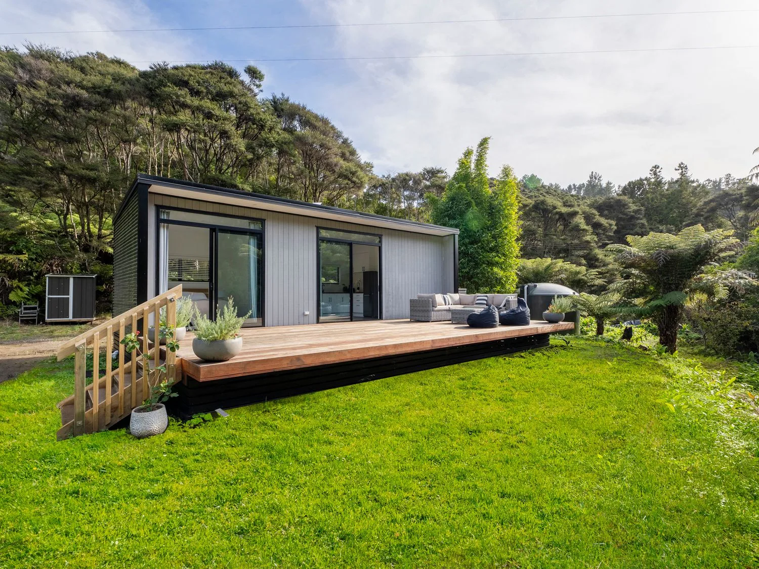 A modern cabin with a wooden deck and outdoor seating sits beside a green lawn.