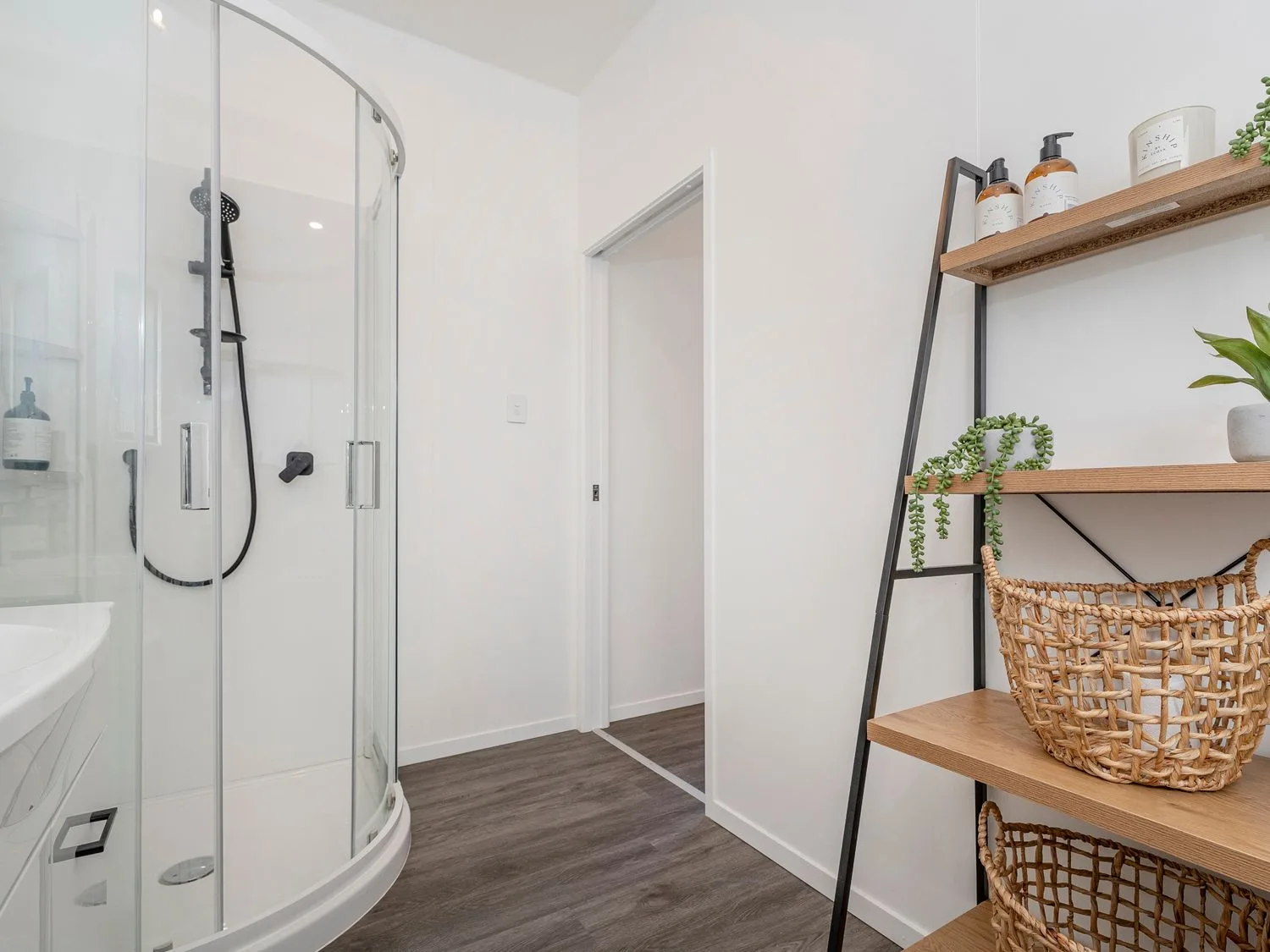 A bathroom with a glass shower and open wooden shelving.