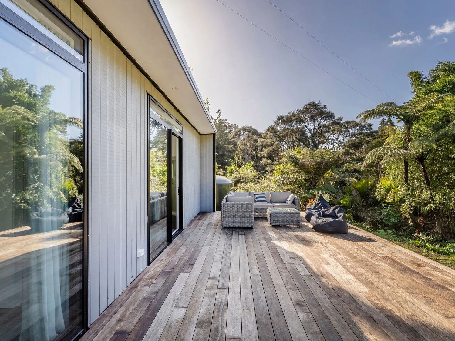 A wooden outdoor deck with a sofa set and bean bags surrounded by trees at Valley Hideaway - Kuaotunu Holiday Cabin in Kuaotunu