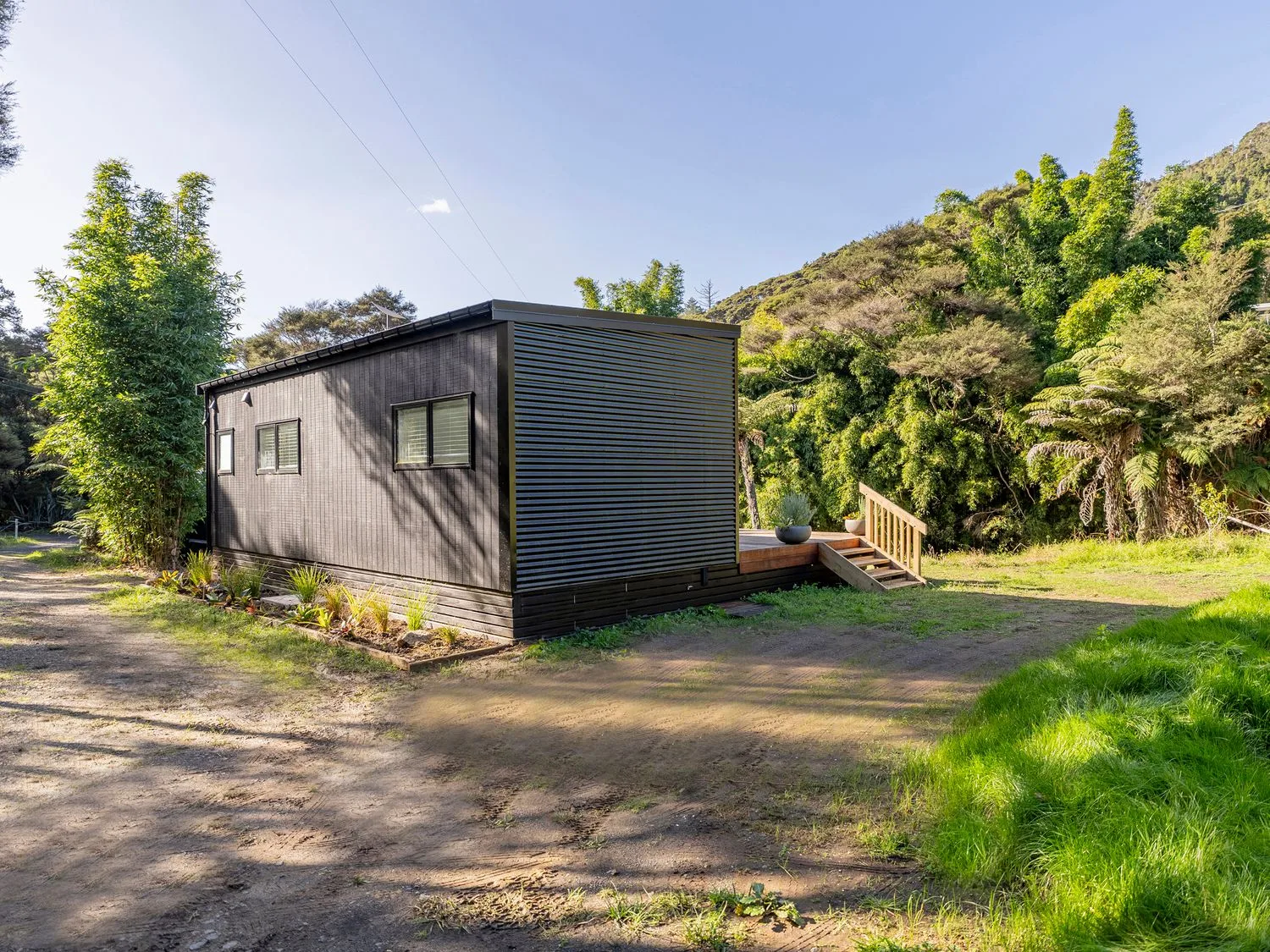 A dark cabin with windows and a small deck sits beside a grassy, tree-lined hillside.