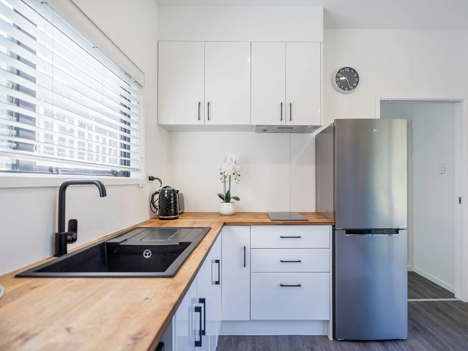 A modern kitchen with a wooden countertop a black sink and faucet white cabinets a stainless steel refrigerator and a wall clock at Valley Hideaway - Kuaotunu Holiday Cabin in Kuaotunu