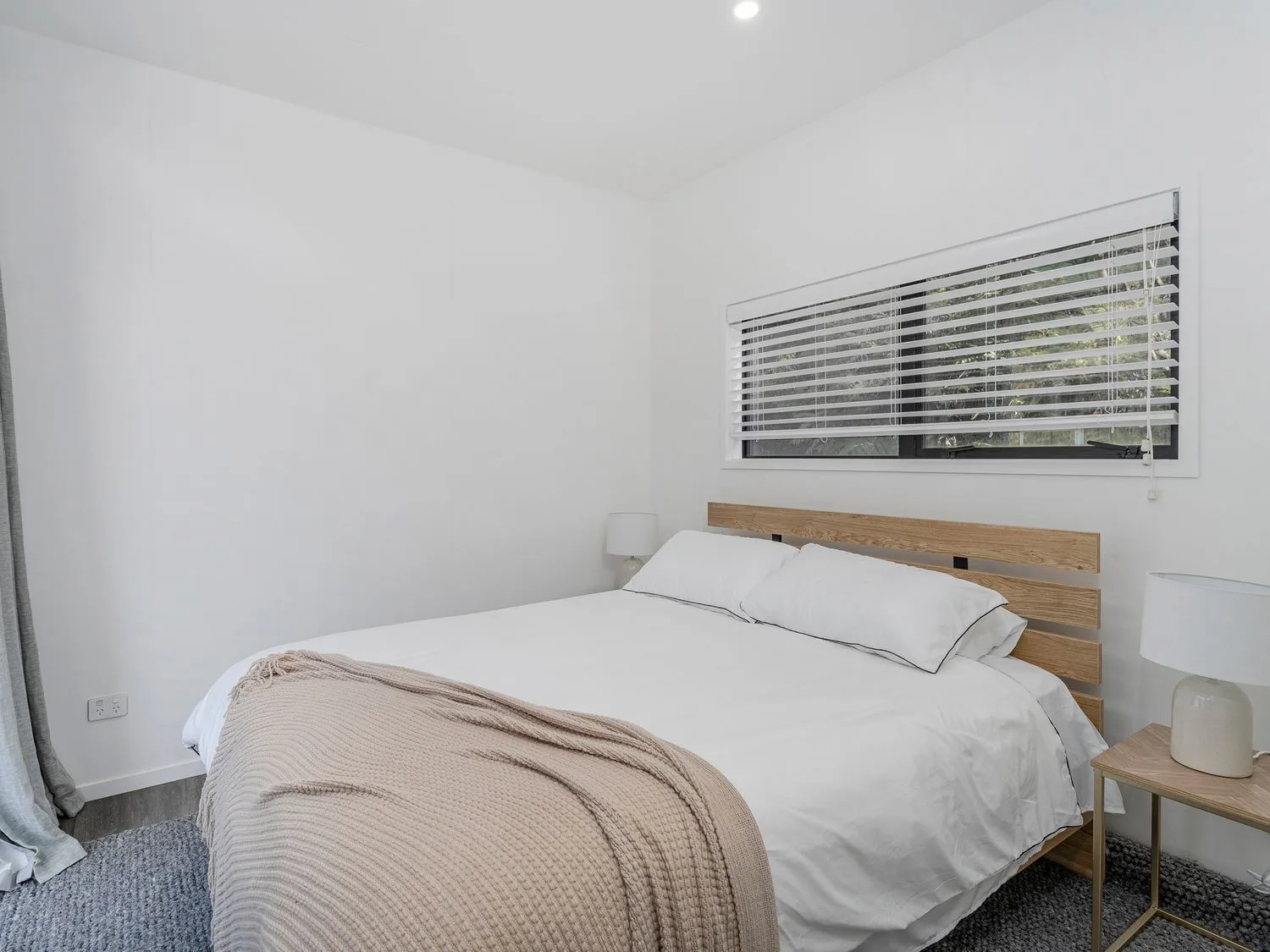 A bedroom with a white bed, wooden headboard, and window blinds.
