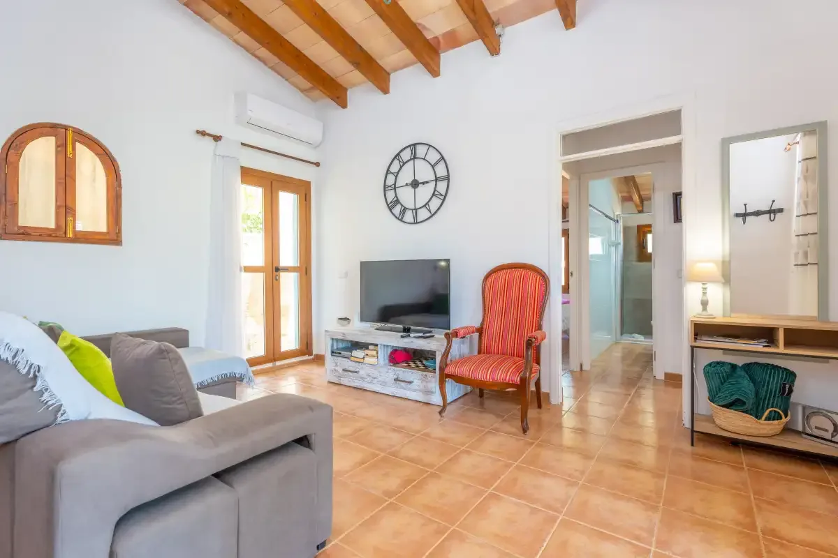 A bright living room with seating, a television, and exposed wooden ceiling beams.