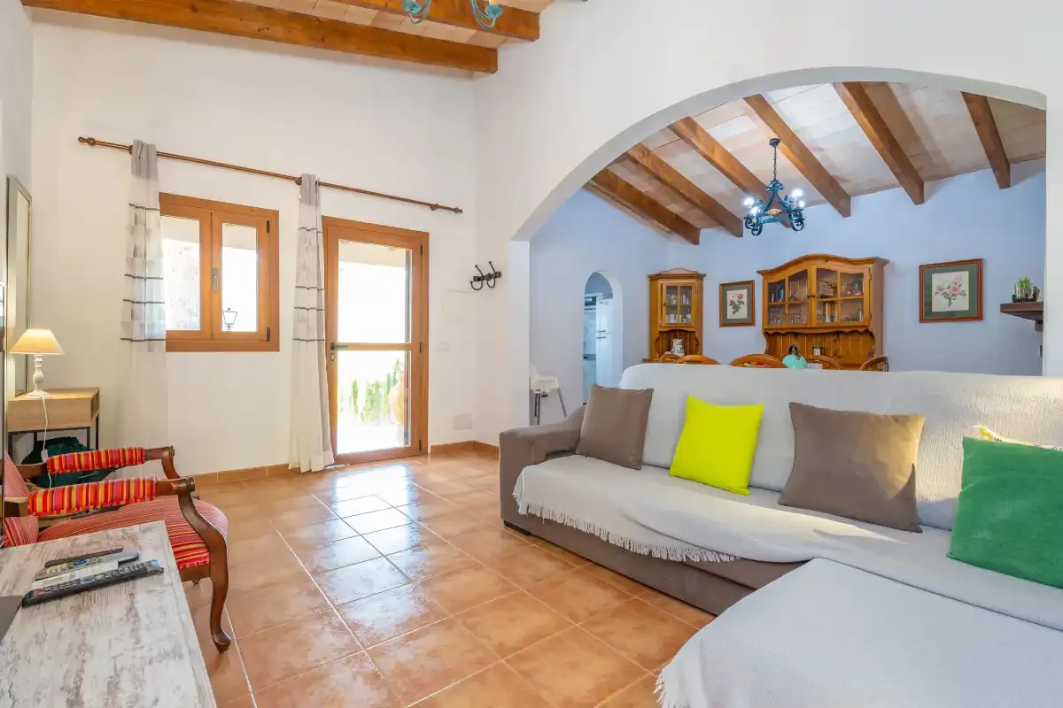 A bright living room with seating, wooden ceiling beams, and a tiled floor.