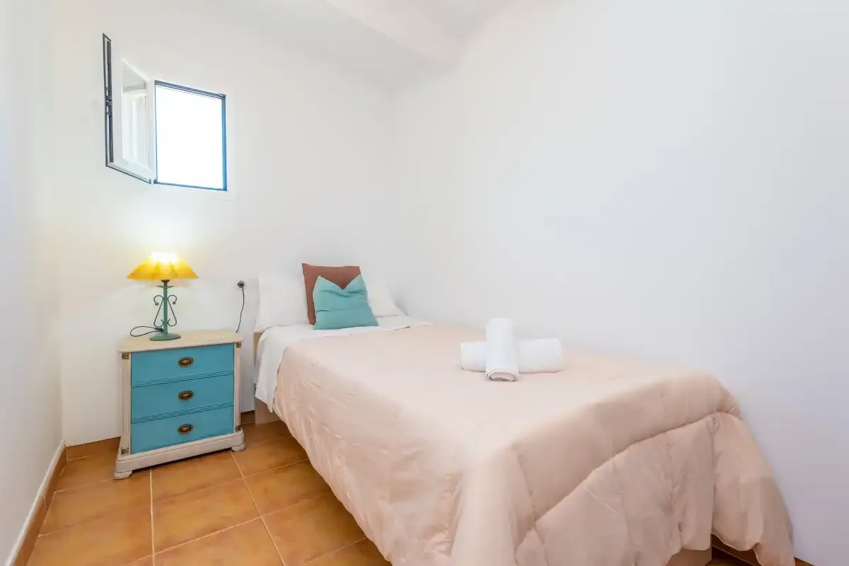 A bedroom with a bed, folded towels, and a small bedside table.